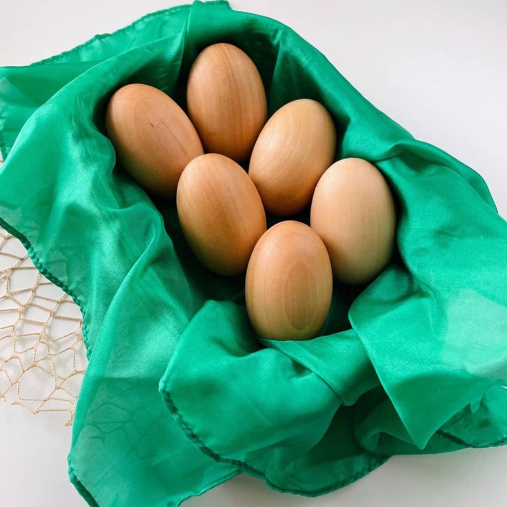 6 wooden eggs sitting inside of a basket lined with a green open ended play silk for kids
