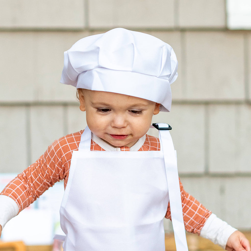 toddler wearing a child's chef apron and hat
