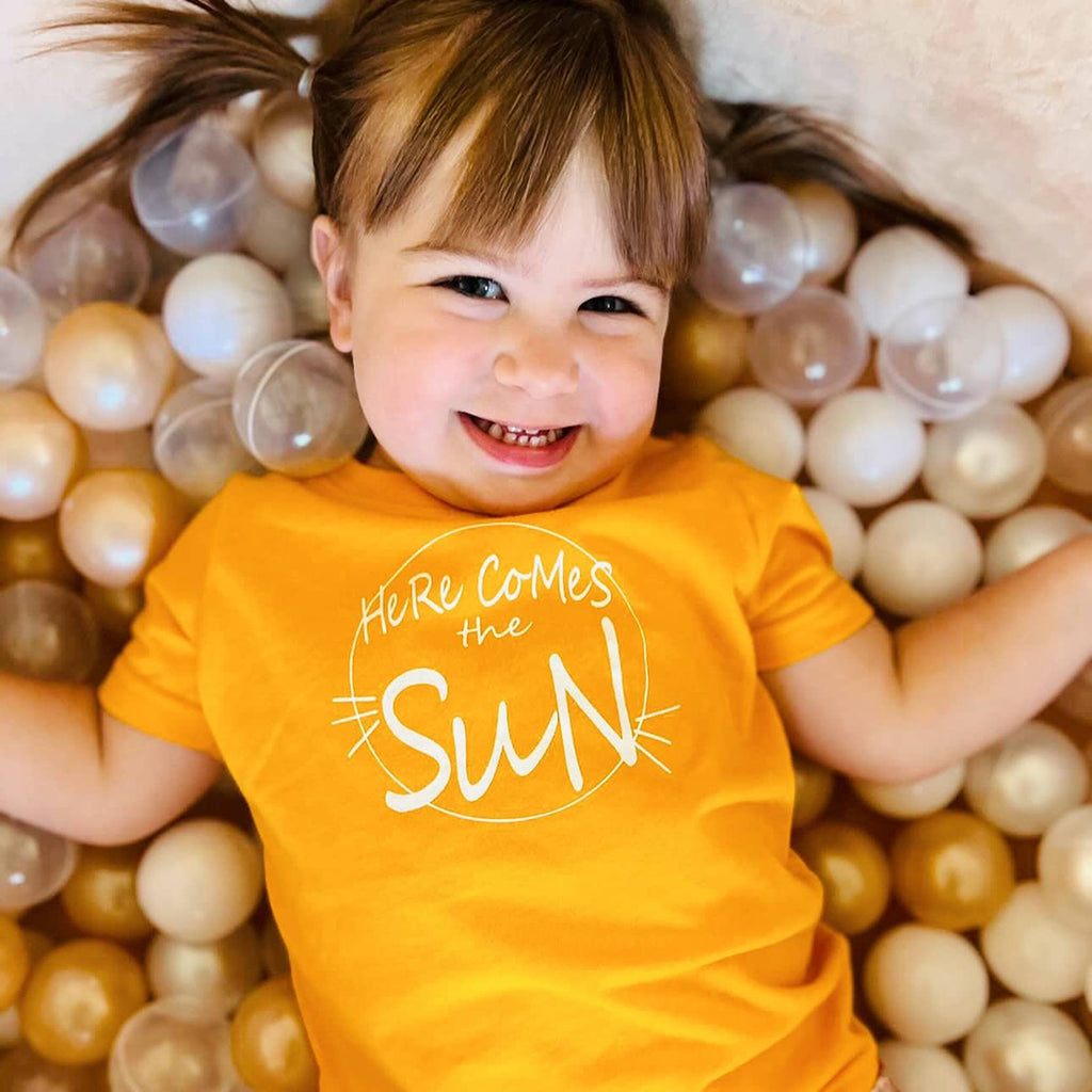 infant girl wearing a yellow Here Comes The Sun onesie