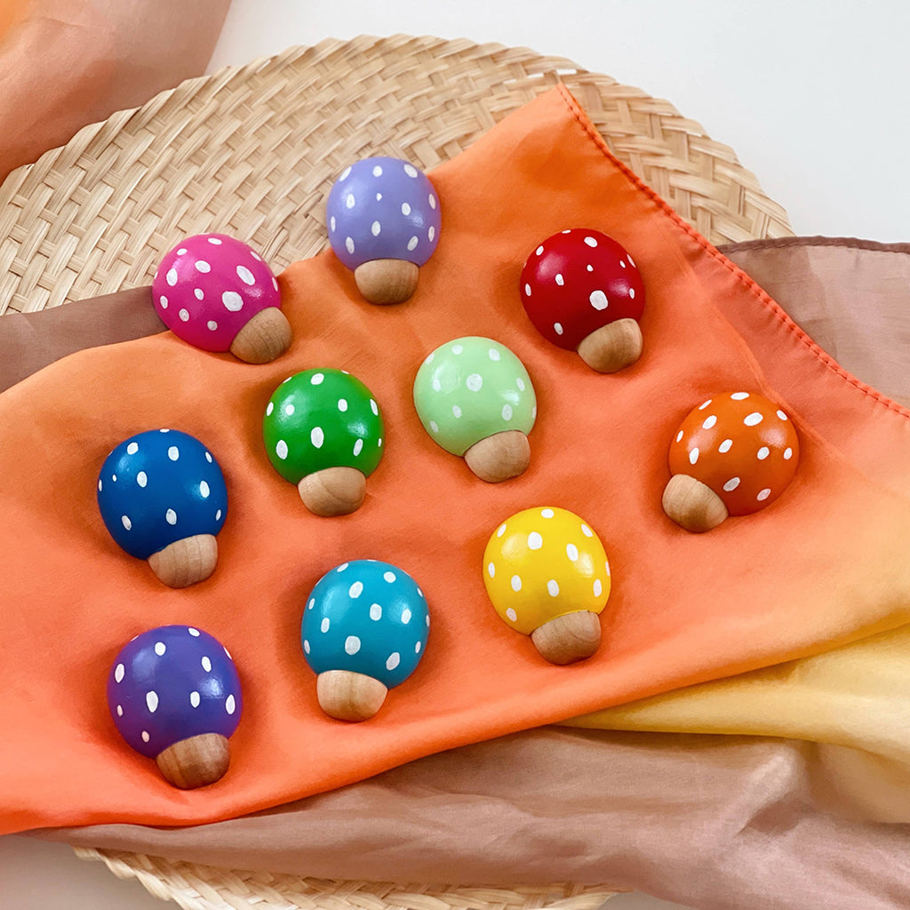 wooden ladybugs sitting on top of an orange colored play silk sensory toy