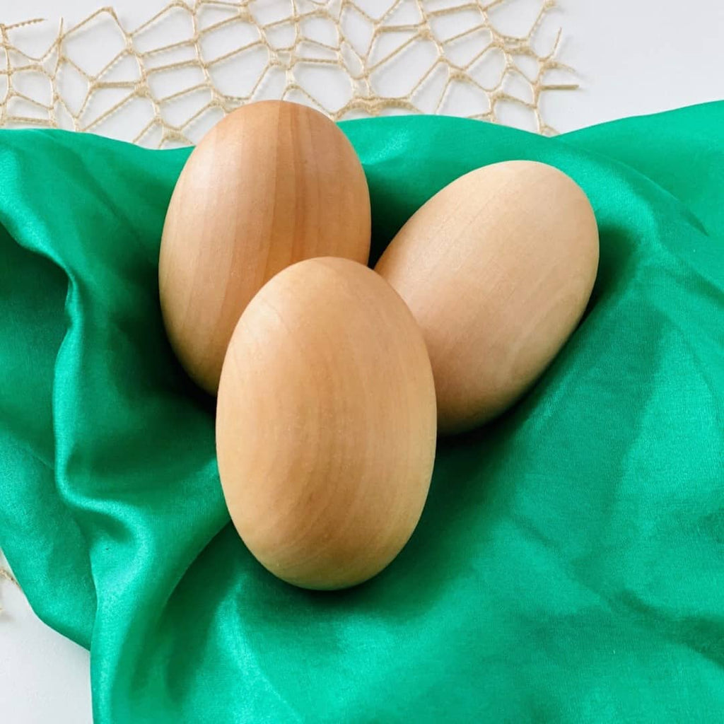 3 large wooden chicken eggs sitting on top of a green play silk for kids open ended play