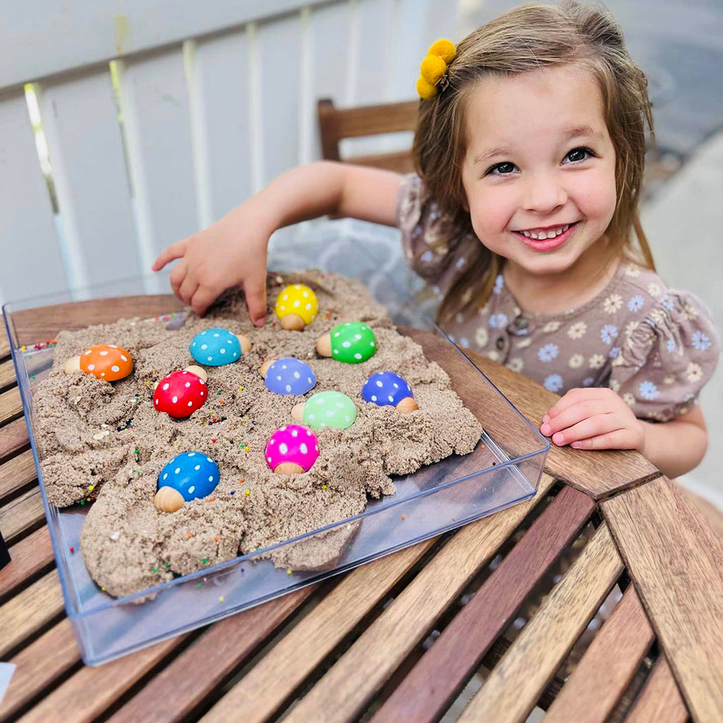 little girl playing with wooden rainbow lady bugs in a sensory bin