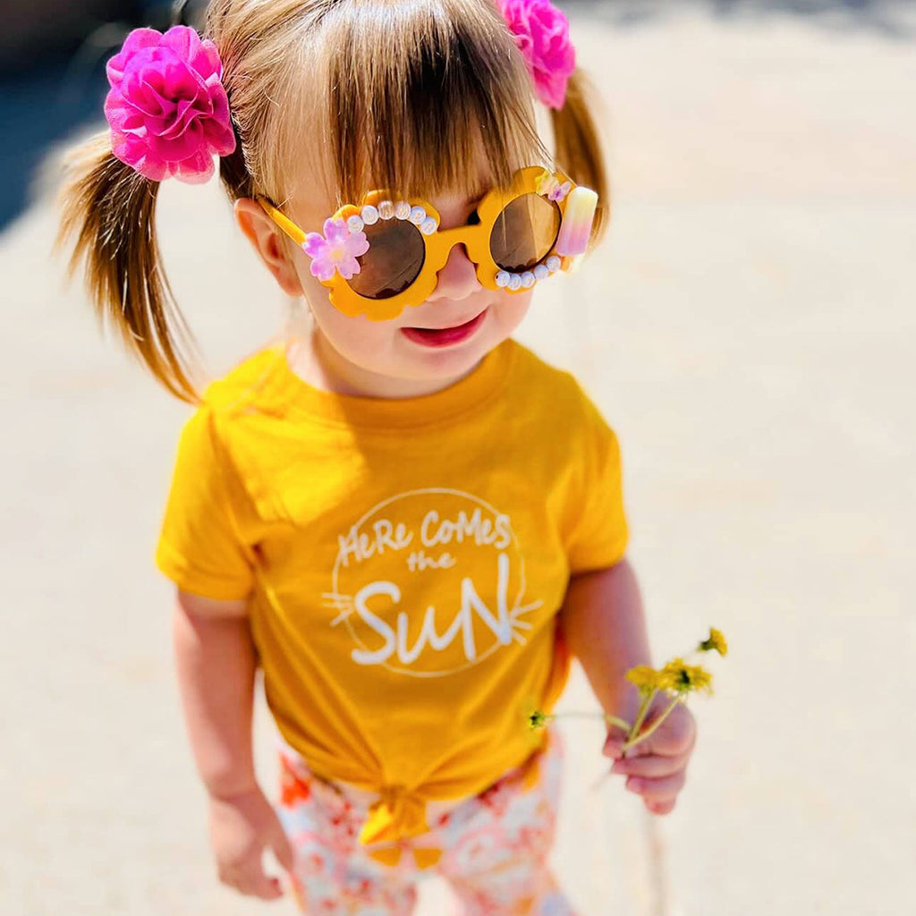 little girl wearing a yellow kids shirt and matching sunglasses