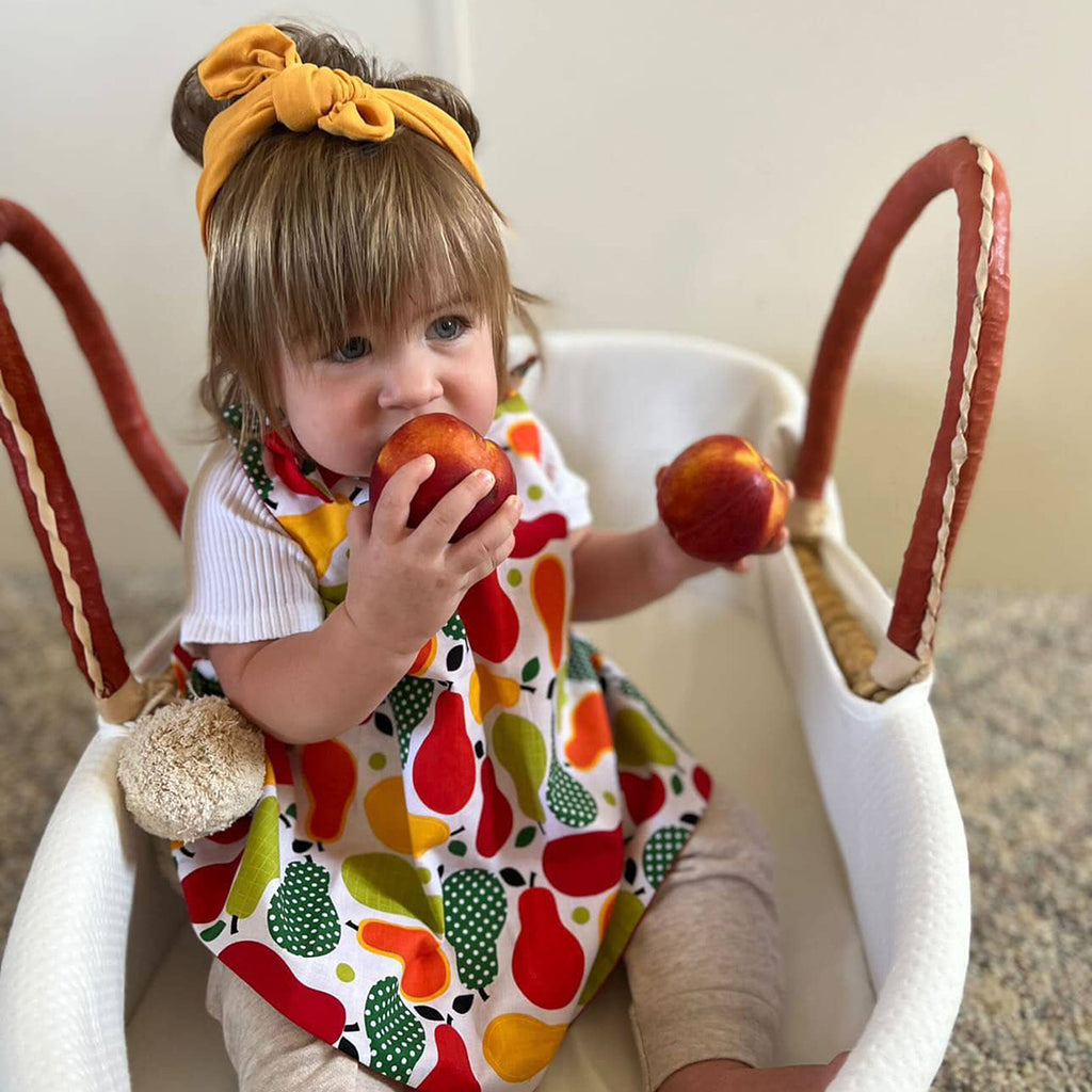 little girl eating fruit while wearing a fruit print fall baby dress