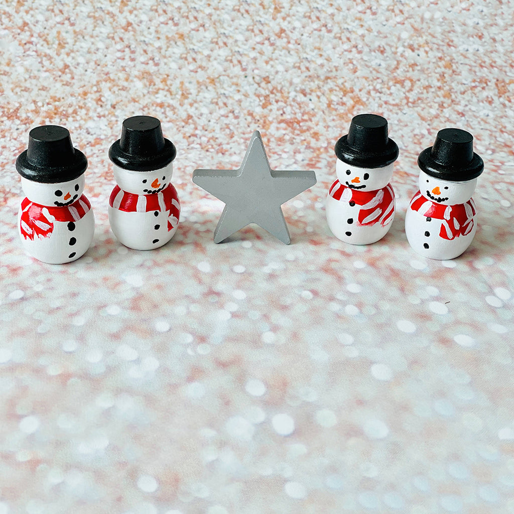 wooden peg dolls painted like snowmen standing next to a silver colored star